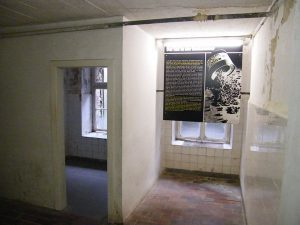 Nebenraum der ehemaligen Gaskammer in der heutigen KZ Gedenkstätte Mauthausen samt Informationstafel zur Gaskammer - Bildquelle: Wikipedia, public domain.
