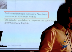 Seminar zum "Veritas-Begleiter", auf der Leinwand: "Die Rheinwiesenlager stellen eine Zäsur in der sogenannten zivilisierten Welt da" (Screenshot eines Imagefilms von "Friedensprojekt")